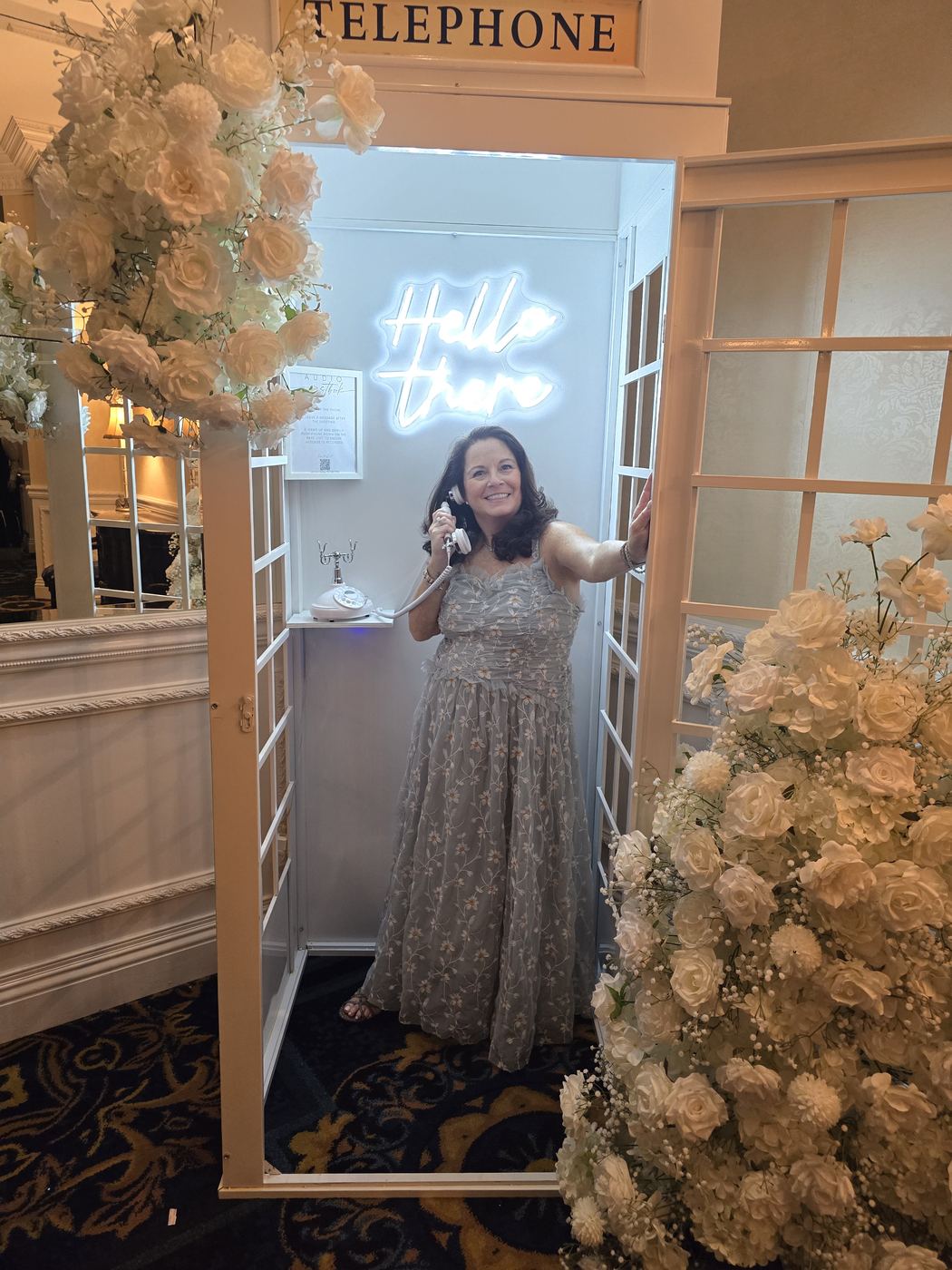 Diane laughing on a vintage telephone in a flower-framed phone booth